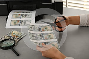 Counterfeiter cutting dollar banknotes with scissors at table indoors, closeup. Fake money concept photo