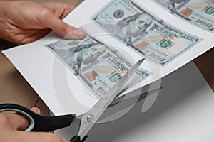 Counterfeiter cutting dollar banknotes with scissors at wooden table, closeup. Fake money concept photo