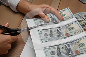 Counterfeiter cutting dollar banknotes with scissors at wooden table, closeup. Fake money concept photo