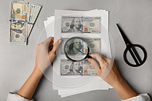 Counterfeiter examining sheet of paper with dollar banknotes at grey table, top view. Fake money concept photo