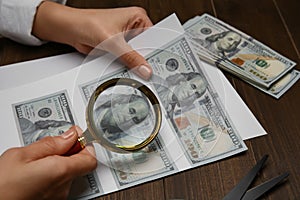 Counterfeiter examining sheet of paper with dollar banknotes at wooden table, closeup. Fake money concept photo