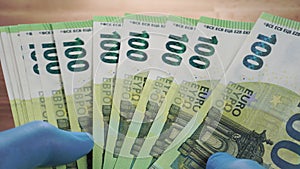 Counting Euro money. Hands in medical protective blue gloves holding European banknotes over a wooden table
