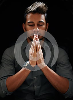 Counting his blessings. Shot of a focused young man standing with his hands together and praying with his eyes closed.