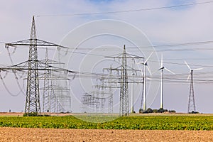 Countless power poles with power lines as well as wind turbines on a field to the horizon