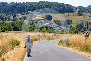 Country asphalt road with adult female hiker walking on left side, German countryside in background