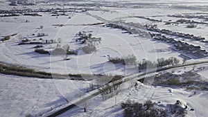 Country asphalt road with driving yellow bus in winter and small village from above. Shot. Aerial drone view in cold