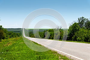 Country asphalt road in summer with green grass and trees on the roadsides against the blue sky. Sunny day background