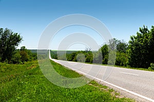Country asphalt road in summer with green grass and trees on the roadsides against the blue sky. Sunny day background