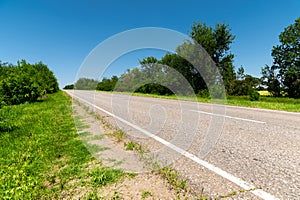 Country asphalt road in summer with green grass and trees on the roadsides against the blue sky. Sunny day background