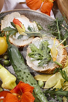 Country breakfast concept with bread, kitchen garden vegetables, herbs and edible flowers, close up