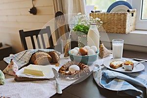 Country breakfast on rustic home kitchen with farm eggs, butter, wholegrain bread and milk.