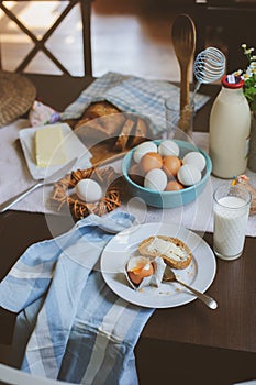 Country breakfast on rustic home kitchen with farm eggs, butter, wholegrain bread and milk.