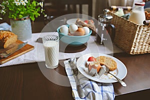 Country breakfast on rustic home kitchen with farm eggs, butter, wholegrain bread and milk.