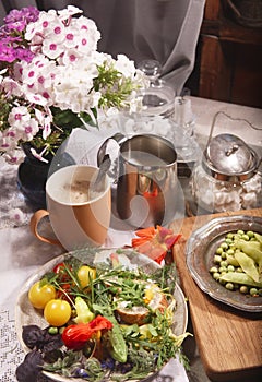 Country breakfast still life with bread, kitchen garden vegetables, herbs and edible flowers, coffee and milk