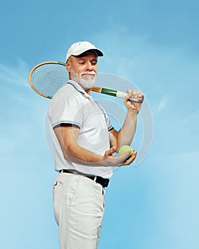 Country club. Portrait of handsome senior man in stylish white outfit posing with tennis racket over blue background