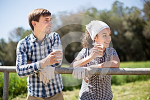 Country couple of farmers drink milk in field near fenc