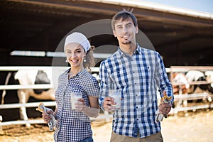 Country couple of farmers posing with glass of milk at cowfarm