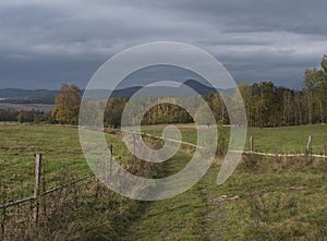 Country dirt road at meadow with autumn colorful forest and trees and hills, moody sky. Landscape in luzicke hory mountain