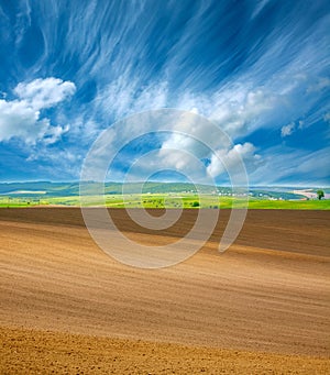 Country dry plowed earth agricultural green farmland on blue sky