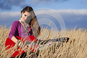 Country girl playing an acoustic guitar in field against blue cloudy sky background