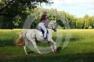 Counrty girl riding horseback on a meadow against woods photo