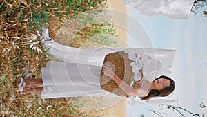 Country lady taking linen from rope at summer field vertical. Woman put laundry