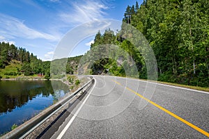 Country landscape with lake's shore and empty highway road.