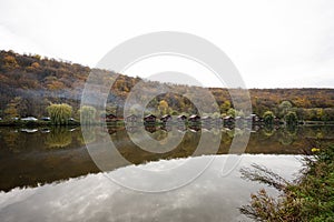 Country landscape. Wooden houses with smoke on the lake. Reflections of a building in the water on a autumn day