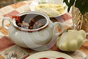 Country outdoor still life with tureen with roasted meat, patisson, mashed potato on the table close up photo
