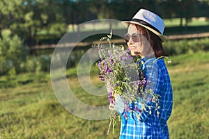 Country portrait of an adult beautiful woman in hat with bouquet of wildflowers