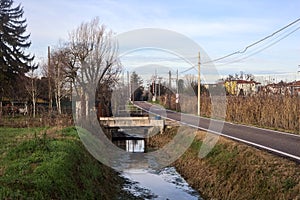 Country road bordered by a stream of water on a cloudy day in the italian countryside