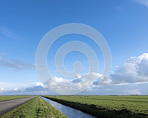 Country road and canal between vast expanse of meadows in dutch eempolder in holland