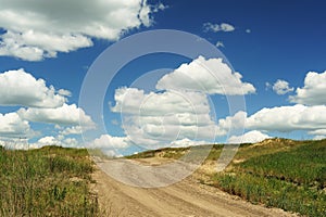 Country road ending in blue sky with big cumulus clouds