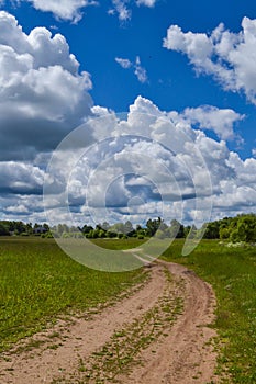 Country road through the field. Sky with clouds