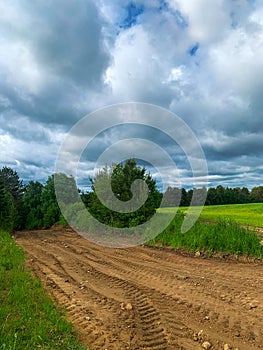 Country road by fields. Stormy deep blue sky and white clouds. Natural landscape background