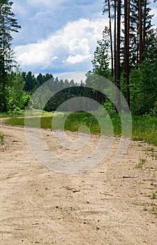 Country road in the forest and blue sky with clouds in Latvia in summer.