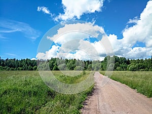 Country road through a green field on a sunny day with clouds.