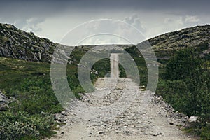 Country road among green hills and lakes on a cloudy day.