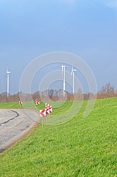 Country Road, green meadow and three wind turbines on the blue sky