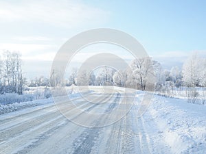 A country road leading among frozen trees on a sunny winter day.