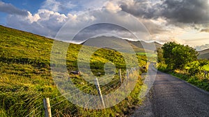 Country road leading toward Carrauntoohil mountain in MacGillycuddys Reeks mountains at sunset