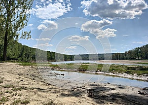 Country road with a rain puddle. The shore of the blue river. Forest on the island. Blue sky with thunderclouds. Moldova