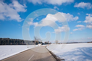 Country road in rural winter landscape, blue sky with clouds
