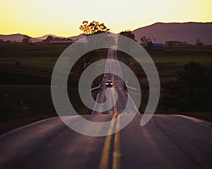 Country road at sunset with car coming