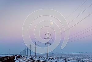 Country road through the winter fields under the moon and wire posts