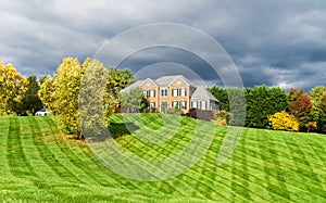 Country two-story brick house for one family with a large green lawn and shrubs. Landscape on an autumn day with low clouds