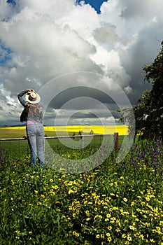 Country womanat farm gate watches the clouds over golden crops and fields