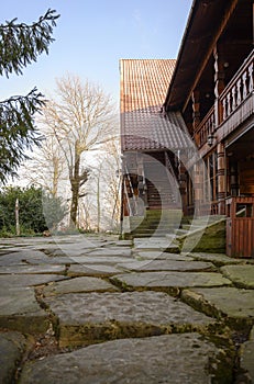 A country wooden house with a carved balcony and a paved courtyard