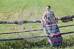 Countrygirl in light dress standing near village fence