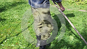 Countryman mows green grass by scythe on backyard lawn